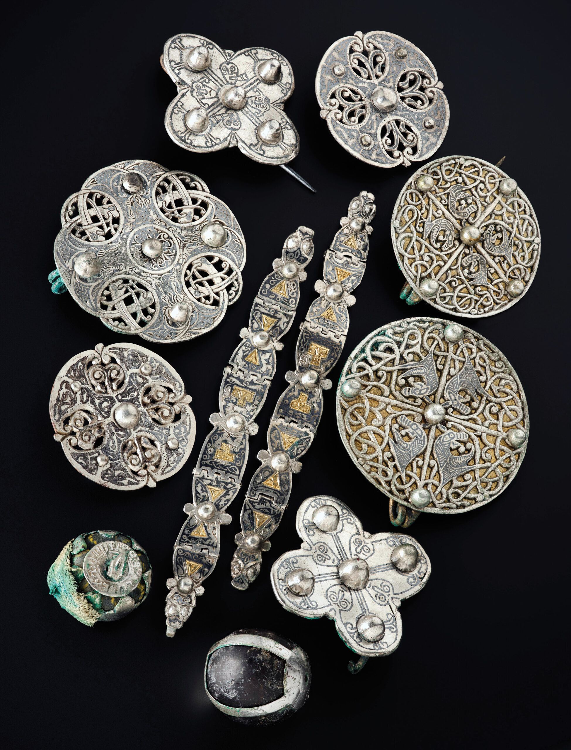 below Anglo-Saxon metalwork recovered from inside a lidded vessel in the Galloway Hoard, including seven brooches, a pair of multi-hinged straps, a ‘relic’ pendant made from a bead enclosed in silver and a perforated coin (bottom left), and a rock crystal sphere in a broken silver pendant-fitting (bottom centre).
