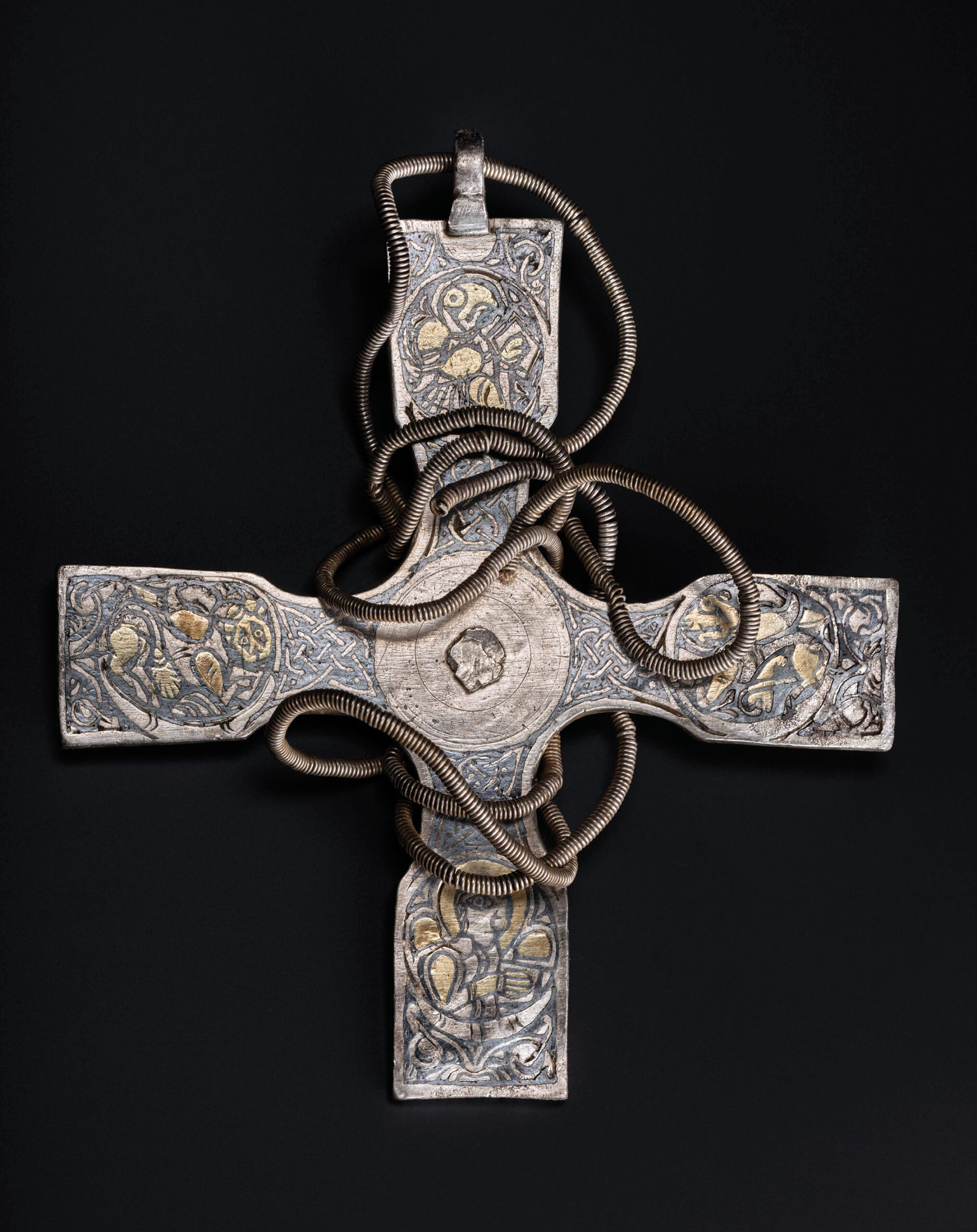 below A silver pectoral cross, decorated with gold and niello, found in the top layer of objects with its spiral chain wrapped around it. The four gospel writers are represented in the four arms of the cross.