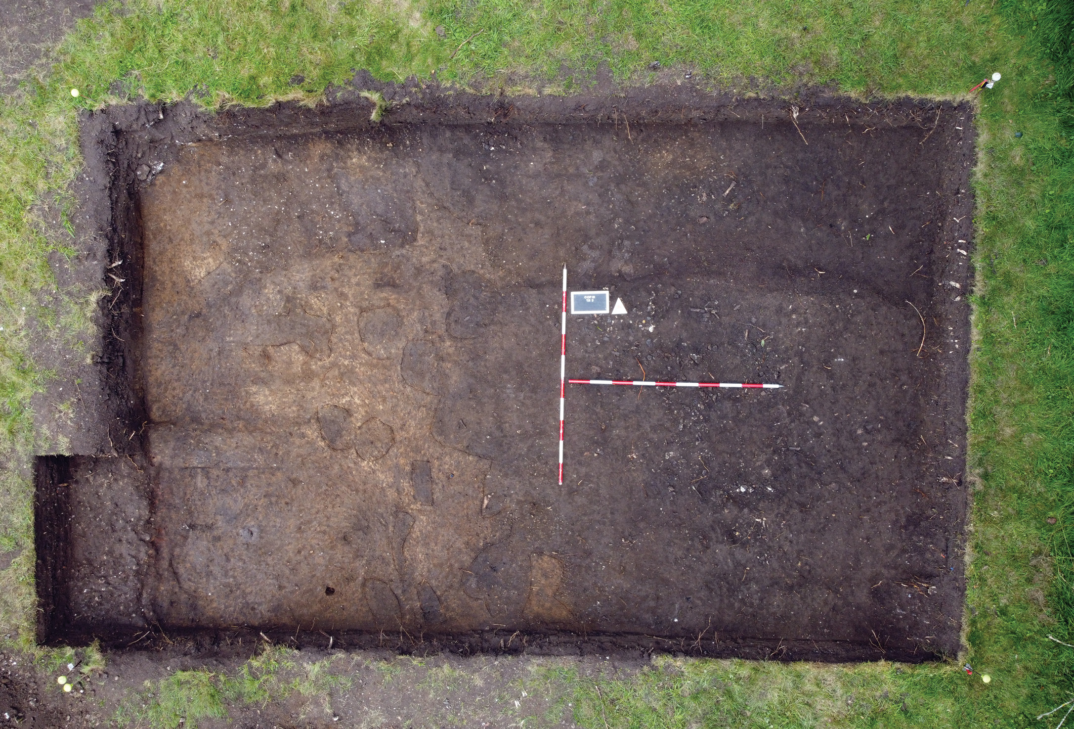 above An extensive midden spread, represented by dark material strewn with fragments of animal bone, covers more than half of this trench. Post-holes cut into the yellow natural geology can be seen to its left.