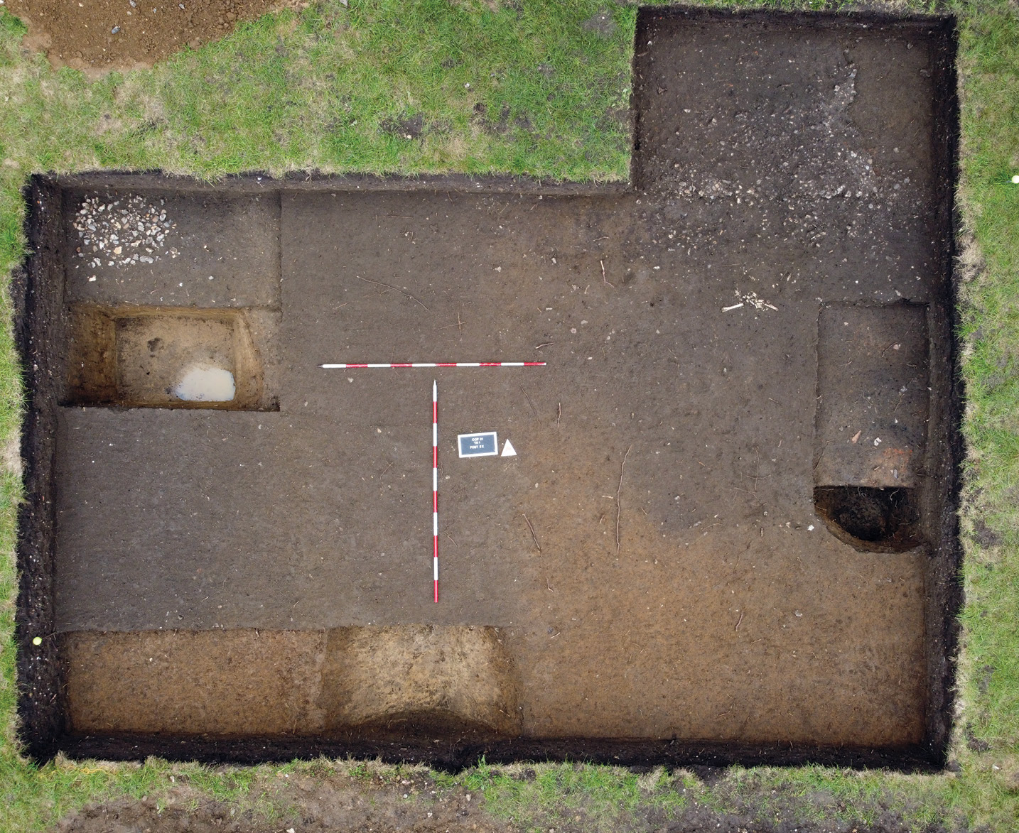 below This trench preserves a portion of a metalled surface/trackway in its top right area. Such routeways represent significant investment in infrastructure on the site. Partially excavated pits (shown extreme left and right) and a section of ditch (bottom) can also be seen.