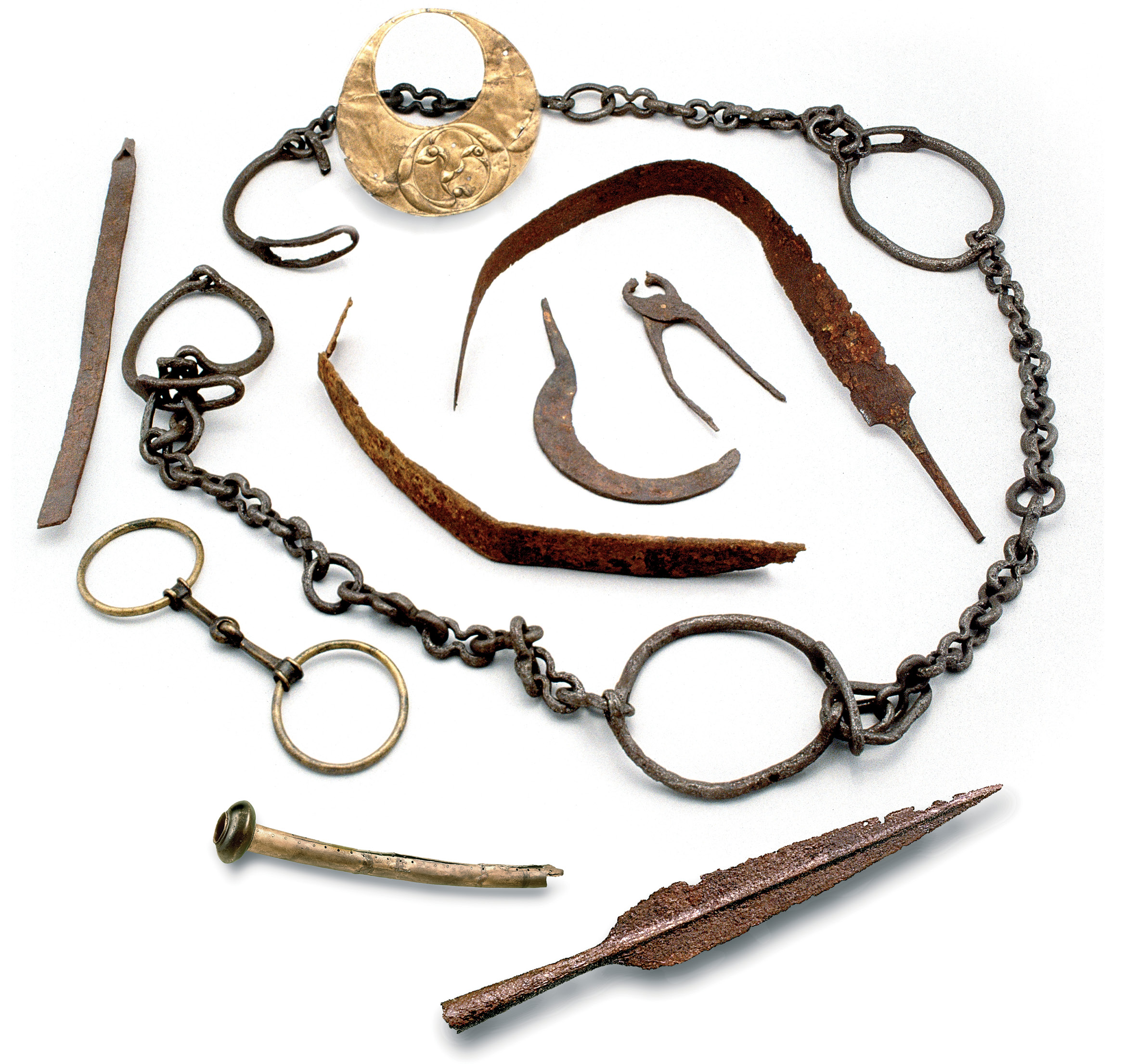 above The haul of Iron Age and Roman metalwork from the Llyn Cerrig Bach. As well as the slave chain, the finds include a crescent-shaped plaque with a decorative ‘three-legged’ motif (at the top). A pair of blacksmith’s short-gripping tongs and a sickle, circled by two deliberately bent sword blades (centre), and a spearhead, a horn fragment, and looking like a pair of handcuffs a bridle bit that would have been attached to a horse’s reins (bottom right to left).