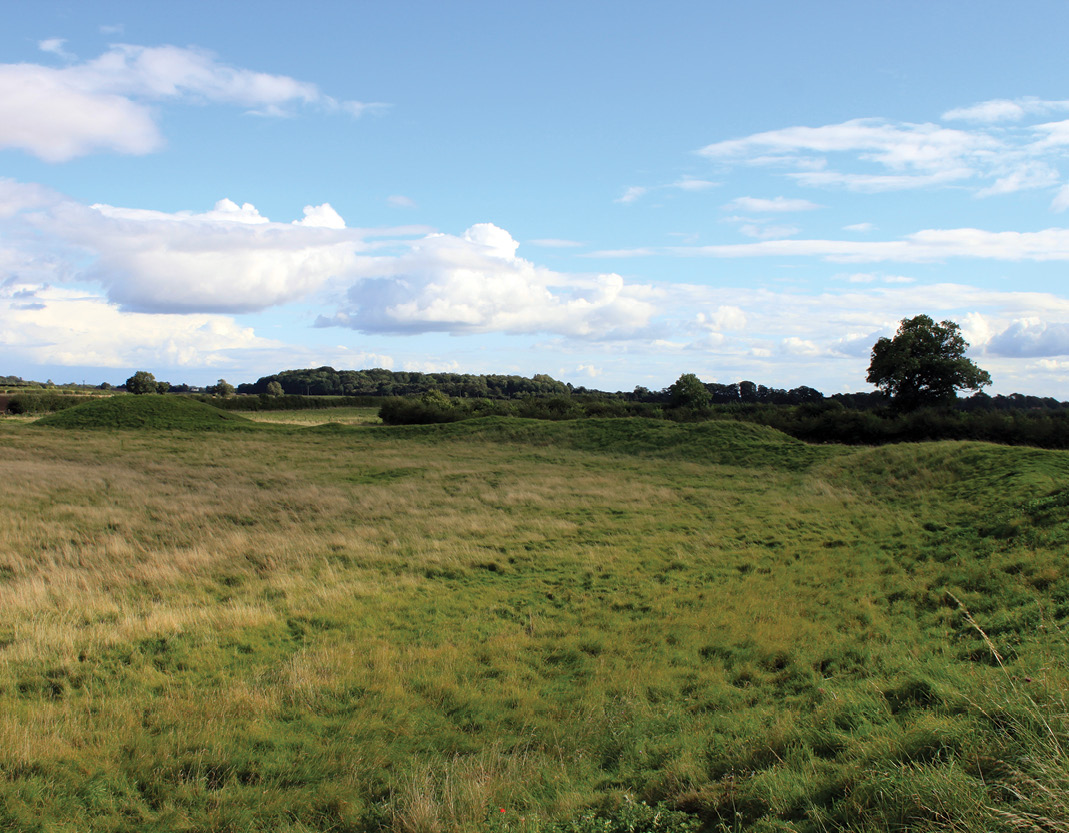 below The circular henges are remarkably homogenous in form, suggesting that they were built over a short period of time as a single monument. The ditches of the central henge (left) have largely been filled in, and the banks survive as greatly denuded earthworks, but they still convey a sense of the huge scale of the original work. A section of the southern henge (right), photographed in August 1994, shows the filled-in ditch, which remains greener because of its greater depth and retained moisture.