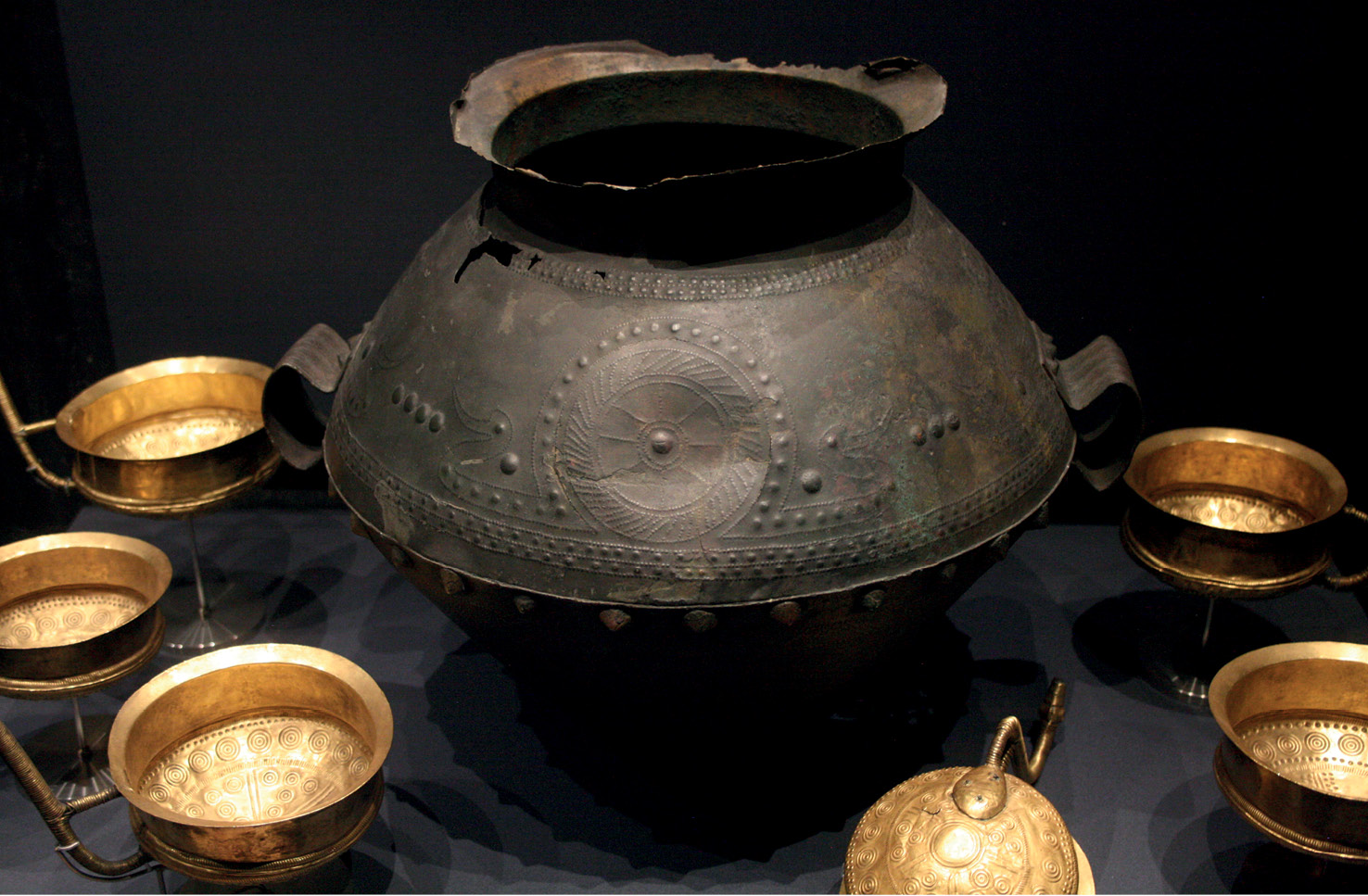 above The locally made gold cups were found with an imported bronze amphora at Mariesminde Mose, Denmark. Both the cups and the amphora bear sun motifs, with a design featuring two birds linked by a boat-shape body and associated with the sun prominent on the amphora.