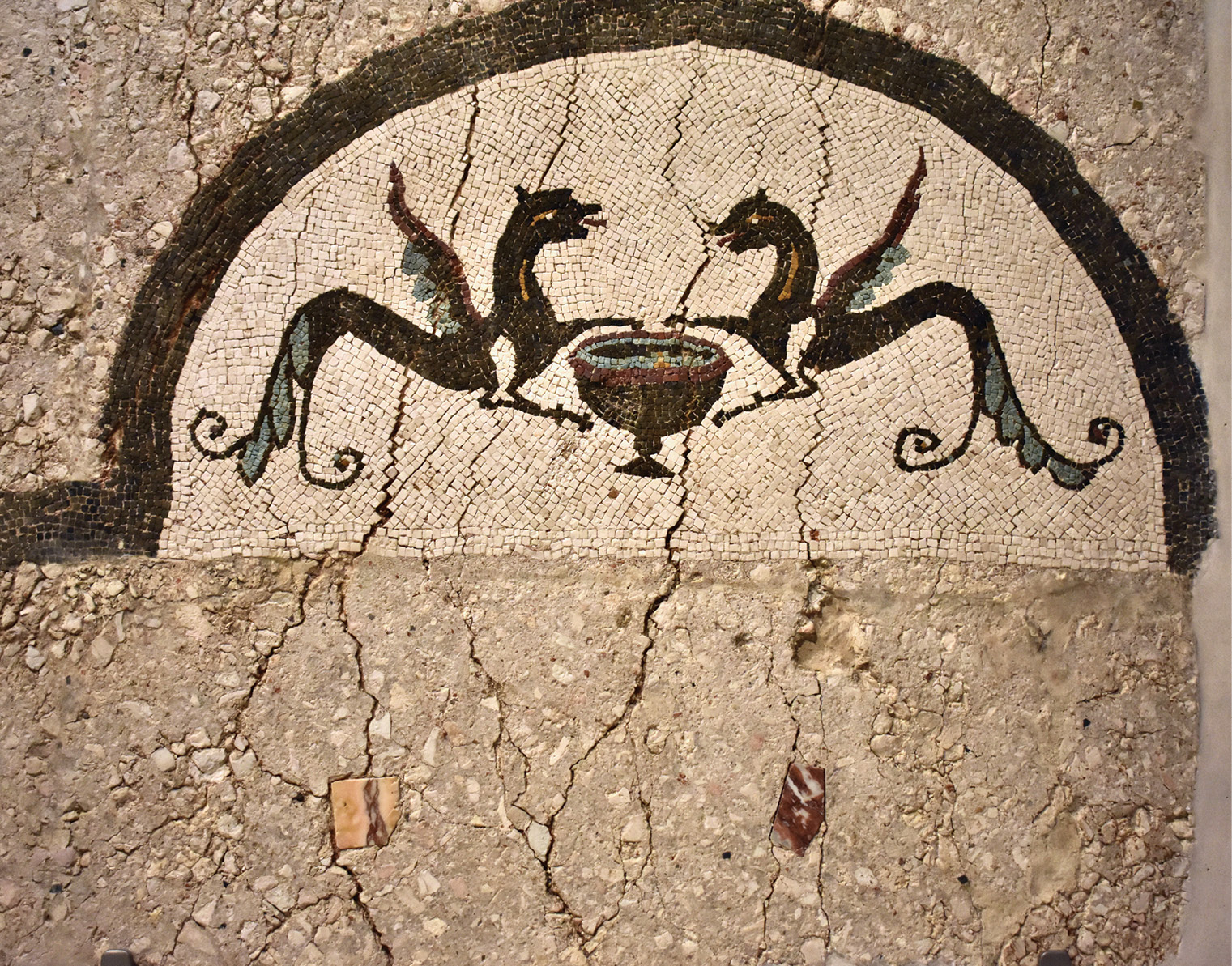 above Detail of a mortar floor with small pieces of marble inlay and also mosaic details, one of the earliest known at Narbonne (25-0 BC). It was found in rescue excavations at the Médiathèque, boulevard Mistral. A pair of griffins, in black tesserae with yellow, turquoise, and white details, face one another across a wine cup. Their back feet have been turned into leafy tendrils. right Detail of a white-ground fresco in the Maison à portiques at Clos de la Lombarde, late 1st century AD. It features birds, a theatre mask, and a red squirrel nibbling a nut while confronting a somewhat alarmed Cupid.