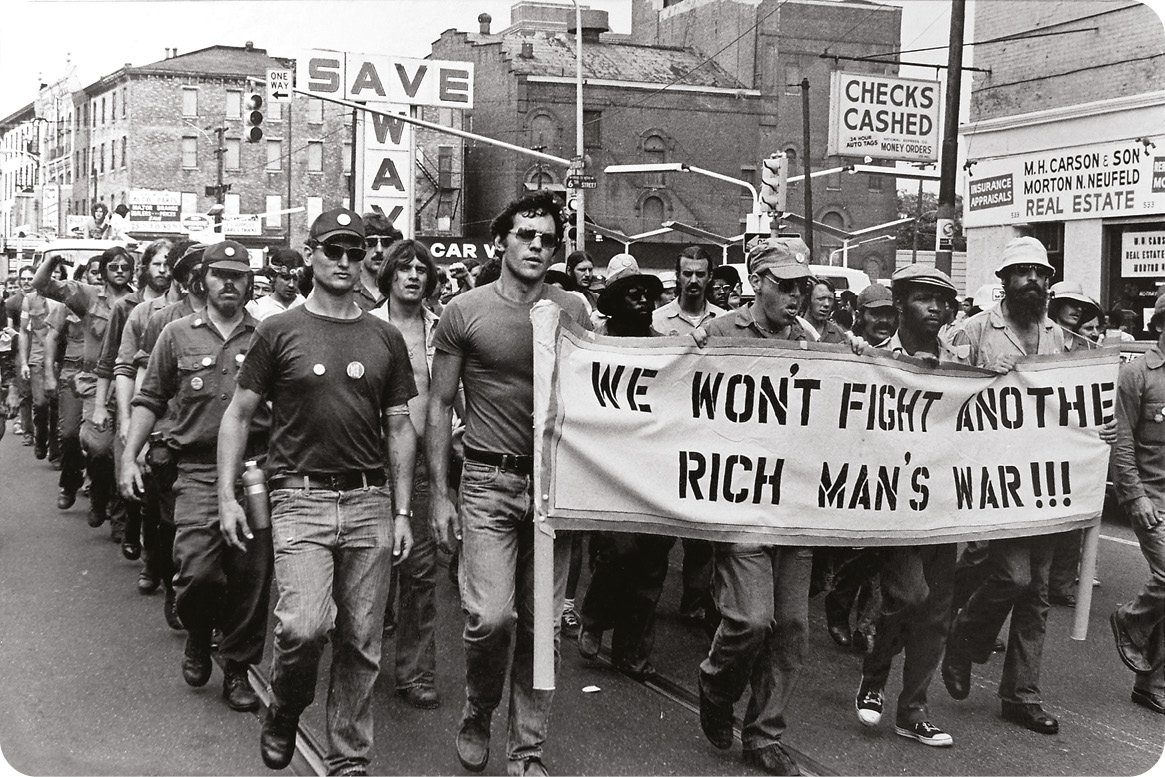 Below Anti-war protestors in the US march against the draft, which disproportionately targeted working-class citizens. right John F Kennedy at a press conference in March 1961. A map depicting the perceived Communist threat sits in the background.