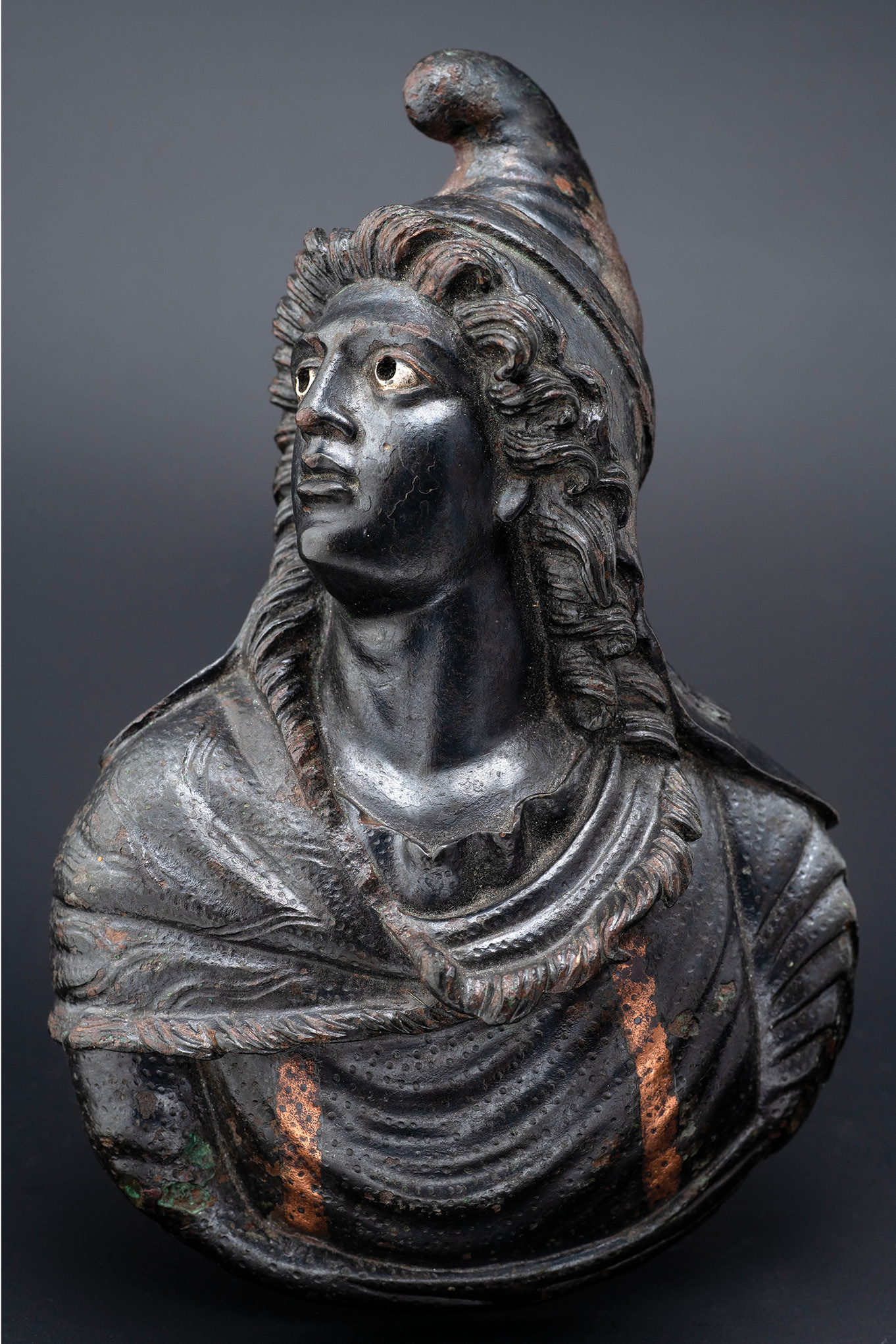 above Bronze appliqué for a piece of furniture with the bust of the god Attis, from the Palaestra, Insula Orientalis II, 1st century AD. Size:16 x 11cm